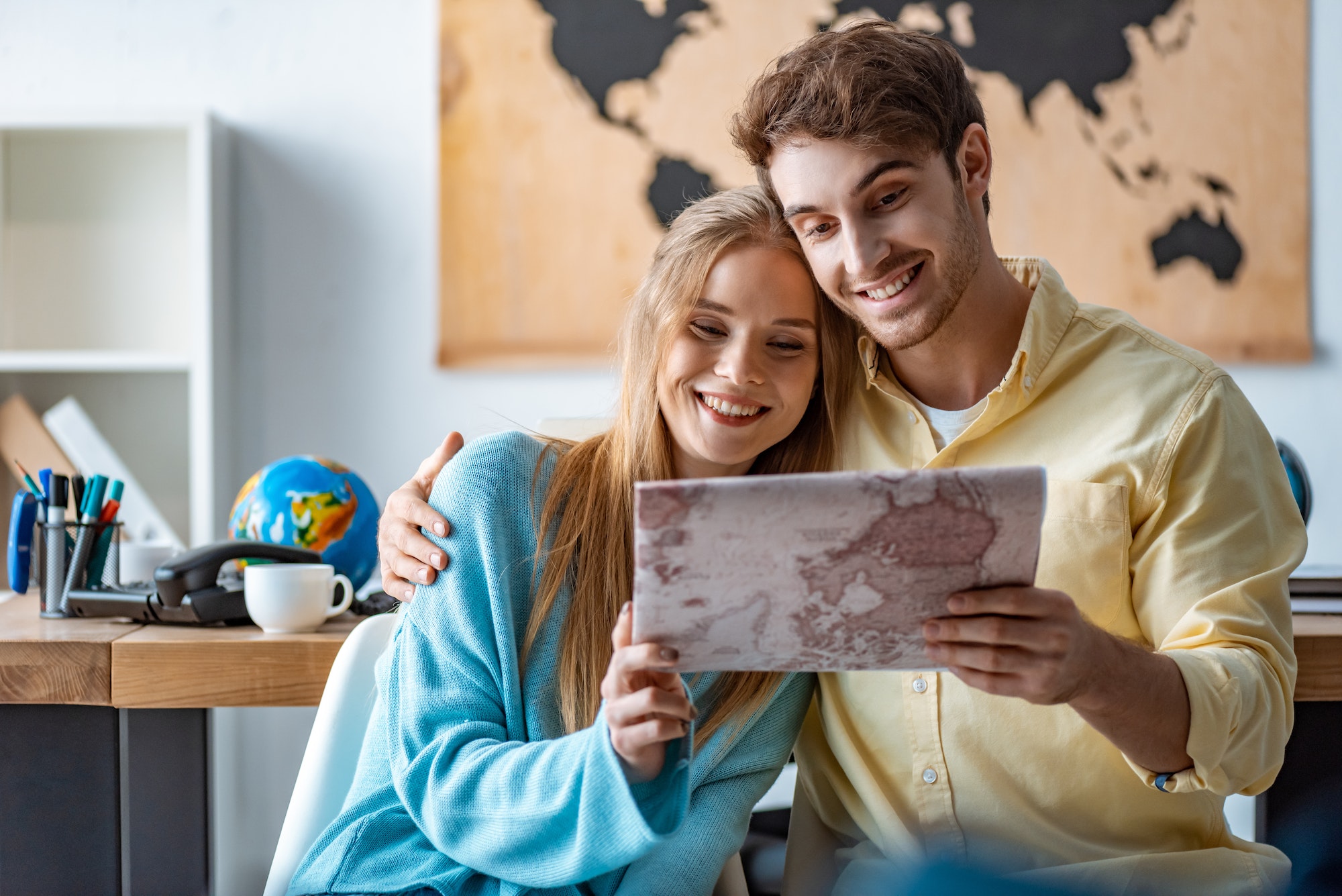 happy couple of tourists looking at map in travel agency